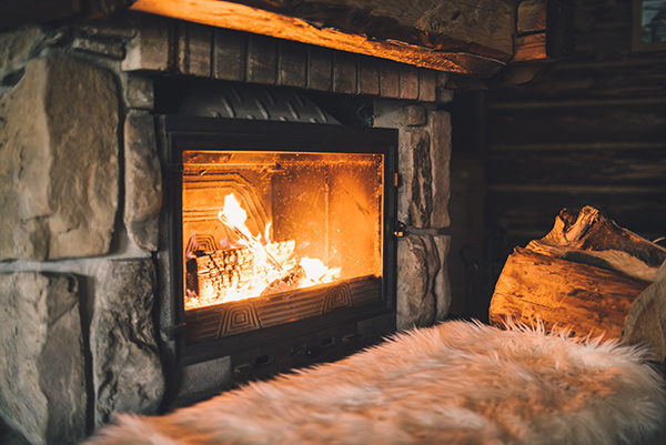 Manasquan chimney service keeps your fireplace safe, fire burning in stone fireplace with fuzzy white blanket in front and firewood on side.