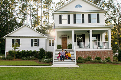 Custom home builder in NJ, family sitting on porch steps of white house with black shutters