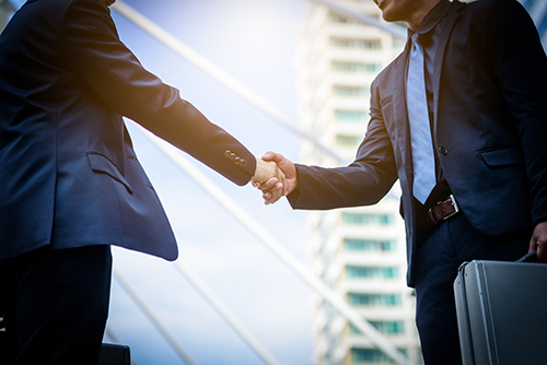 Branch manager and NCR ATM service technician shaking hands in front of a sunny city backdrop